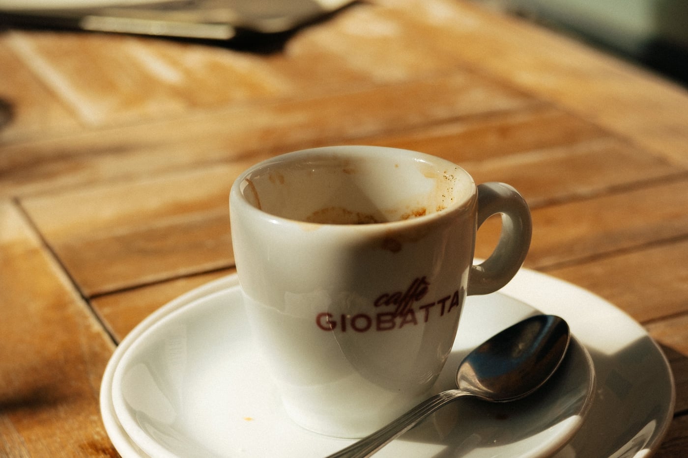 A coffee cup and spoon on a saucer next to a printed receipt on a wooden cafe table