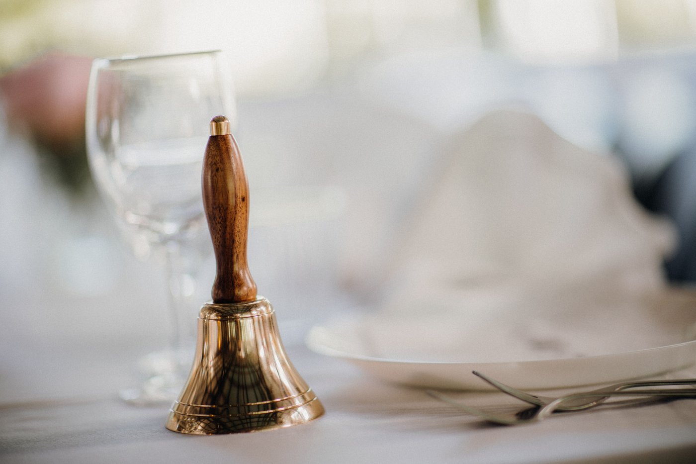 Brass service bell on a restaurant table next to a glass and cutlery