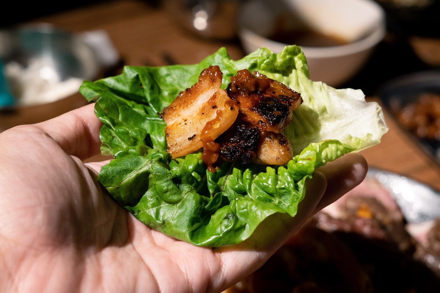 Grilled pork belly with ssamjang on a lettuce leaf held in the palm