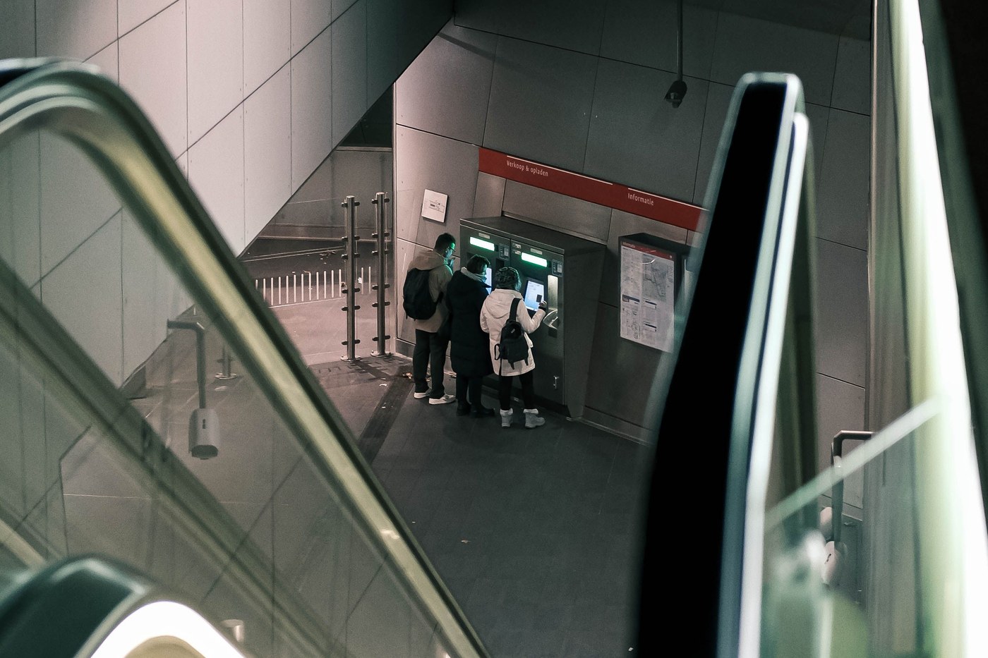 People using a subway ticket machine at the bottom of an escalator
