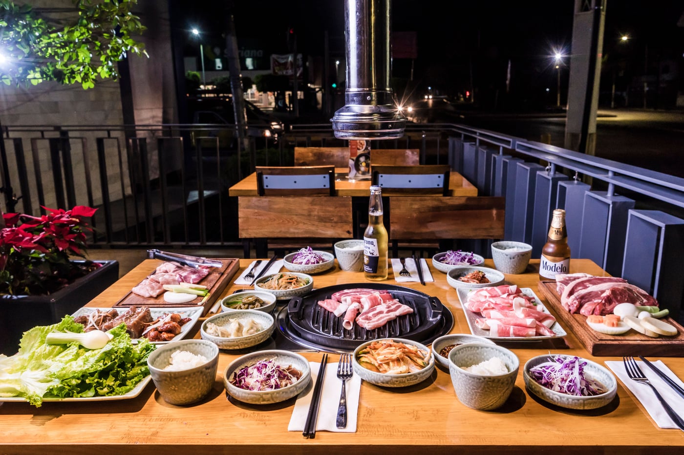 A Korean barbecue table set with grilled meat, banchan side dishes, and drinks