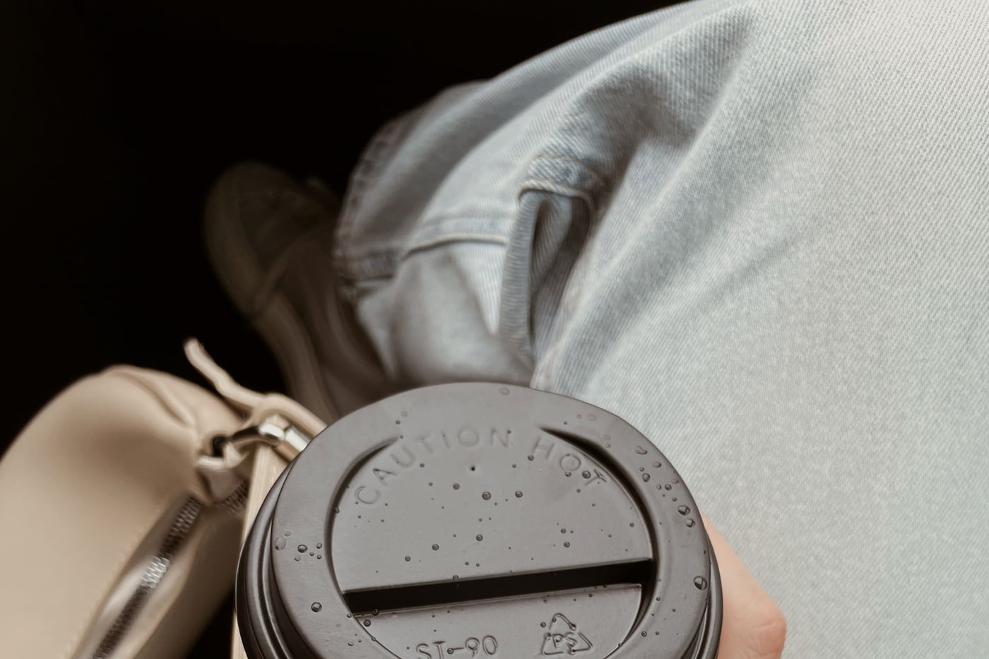 A hand holding a disposable coffee cup with a caution hot lid